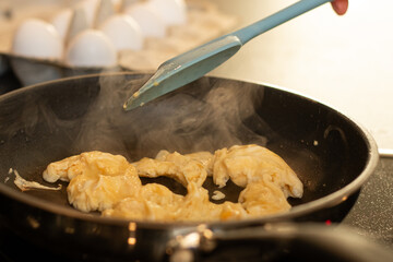Close up of making scrambled omelet egg in a pan, blurred kitchen table background with white eggs