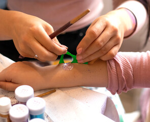 Kid's animator is creating a Shimmering sparkling glitter tattoo on a child's hand at a birthday party. Body art. High quality photo