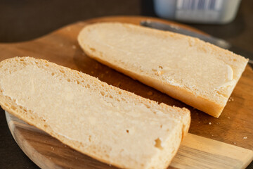 Close up of two slice of white baguette bread on wooden cutting board with butter 
