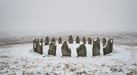 Ethereal stone circle embraced by winter's snowy veil in the misty highland