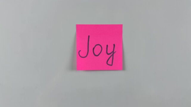 Sticky note with word Joy written on it, pinned on white background. Symbolizes happiness, delight, and positivity. Ideal for celebration and wellness concepts
