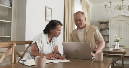 Asian senior couple working together at home, using laptop and writing notes - Powered by Adobe