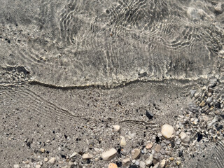 waterline with ripples and small stones in shallow sand. abstract natural composition with assorted pebbles, fluid motion, water surface, abstract