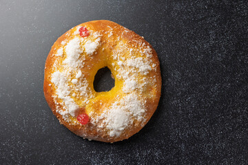 Roscón de reyes, spanish epiphany cake, sprinkled with icing sugar, on dark background