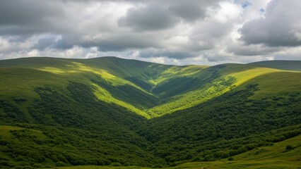 Obraz premium Green mountain range landscape with grassy hills and a cloudy sky.