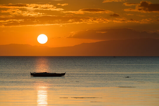 Serene Sunset Over Ocean with Silhoutted Boat and Warm Tones