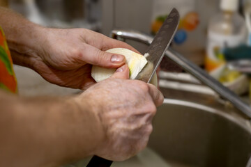 Close-up view of men's hands peeling and slicing onions with knife over sink.