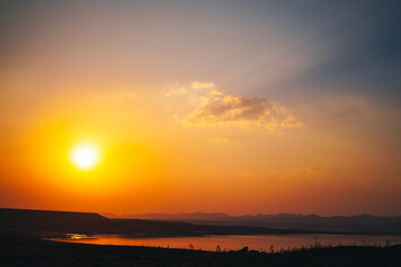 Obraz premium A breathtaking sunset casts golden and orange hues over a tranquil lake, with distant mountains creating a peaceful and scenic backdrop.