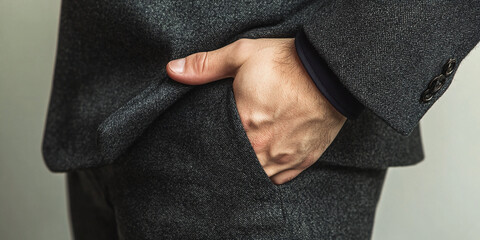 Close-up of a hand in a dark gray textured suit pocket, showcasing fabric detail and male hand, suggesting confidence and professionalism