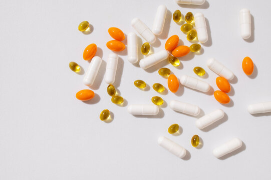 Different capsules vitamins, natural supplements, nutraceuticals on light gray background top view. Tablets, pills close up. Medical pharmaceutical background. Solar lighting