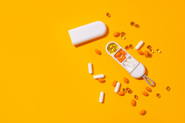 Stylish pillbox, organizer for vitamins, capsules, dietary supplements, tablets on yellow background, top view. Multivitamins, health support, homeopathy. Minimalistic concept. Sunny Summer Shadows