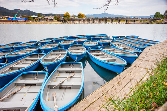 A fleet of blue rowboats docked on the serene Arashiyama River in autumn, Kyoto, Honshu