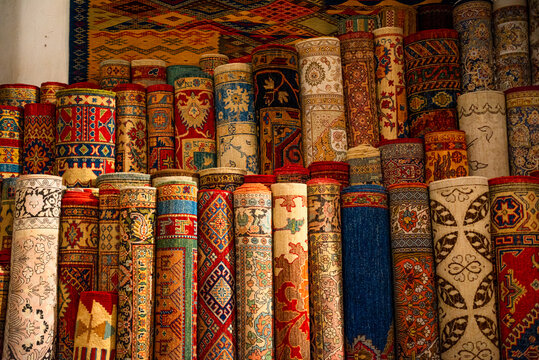 Stacks of vibrant handwoven Moroccan rugs and carpets displayed in a traditional shop in Fes