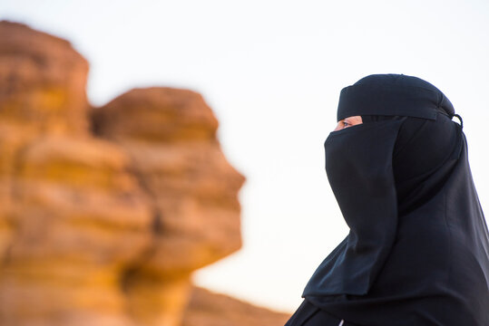 Woman in a niqab at Face Rock, a sandstone rock formation in shape of human head profile, Hegra, UNESCO, AlUla, Medina Province
