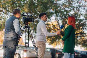 Journalist interviewing businesswoman with cameraman filming outdoors
