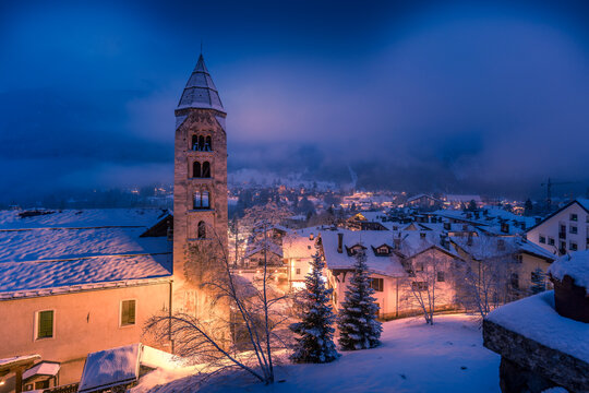 Church of Saint Pantalon and snow covered town centre and mountainous background in winter at dusk, Courmayeur, Aosta Valley, Italian Alps