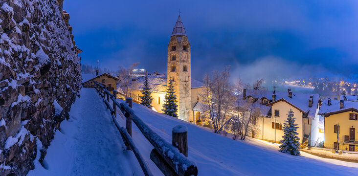 Church of Saint Pantalon and snow covered town centre and mountainous background in winter at dusk, Courmayeur, Aosta Valley, Italian Alps