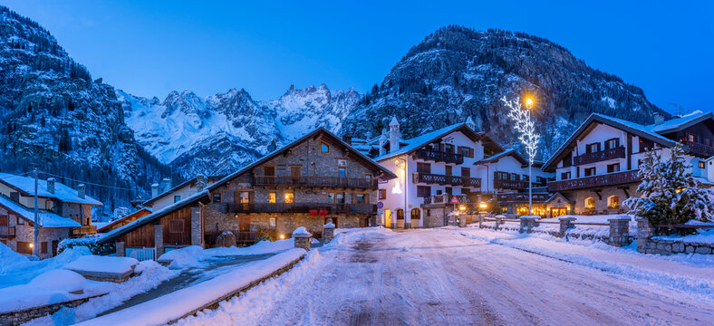 View of town centre and snow covered mountains in background at dusk, Courmayeur, Aosta Valley, Italian Alps