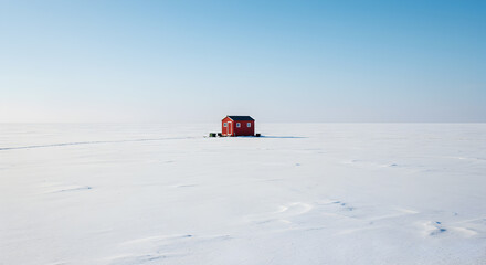 Solitary red cabin on a snowy expanse offers warmth against the cold backdrop