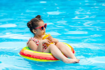 Cute child, little girl in sunglasses spend time in swimming pool on rainbow color inflatable ring, drinks a cocktail. Summer vacation concept. Hotel spa resort advertisement