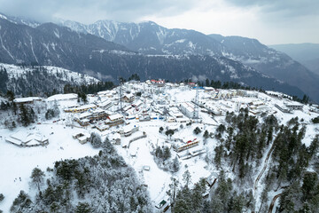 A breathtaking aerial view of Shogran Hill Station blanketed in snow, surrounded by towering...