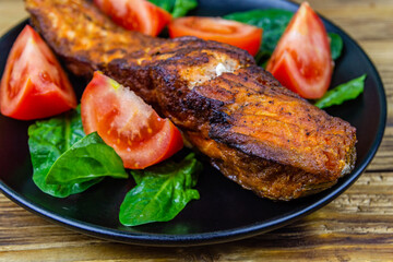 Plate with roasted salmon steak, tomatoes and spinach leaves on a wooden table