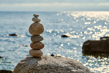 Stack of smooth stones precariously balanced on larger rock by calm seaside, symbolizes balance and...