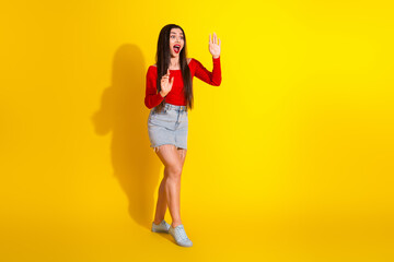 Young woman in a casual red top and denim skirt posing on a vibrant yellow background, showcasing stylish and cheerful fashion