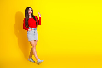 Young woman posing and showing peace gesture surrounded by bright yellow background, highlighting joy and casual summer style