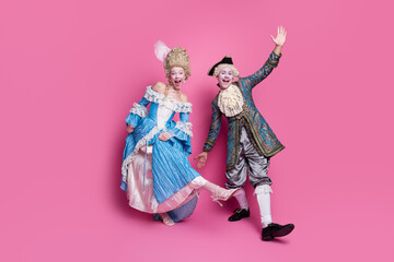 Elegant couple in luxurious baroque costumes posing playfully against a vibrant pink background