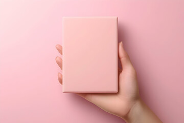 Obraz premium Pale pink gift box held in a hand against a pale pink background