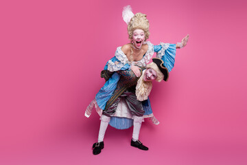 Joyful couple in elaborate historical costumes poses playfully against vibrant pink background, embracing the fun of a theme party