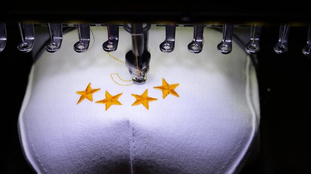 Machine embroidery of stars on a white hat with orange thread. Embroidered baseball cap close-up. 4k 50 fps video.