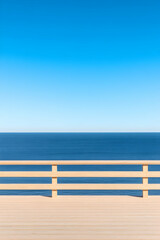 Calm ocean view from wooden deck with railing under a clear blue sky