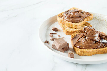 Spreading sweet chocolate cream, cashew, chocolate chunks onto toast on table.
