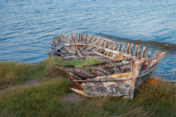 Weathered broken wooden boat remains abandoned by the water shore in natural coastal landscape