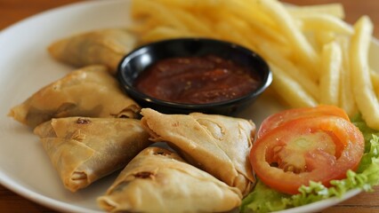 Vegetarian samosas with crunchy fries and fresh salad served with tangy dipping sauce Flavorful Indian snack deep-fried to perfection combining crispiness and rich spices Healthy food concept