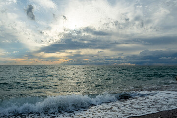 The sound of sea waves crashing on a pebble beach. The setting sun hid behind dark clouds.