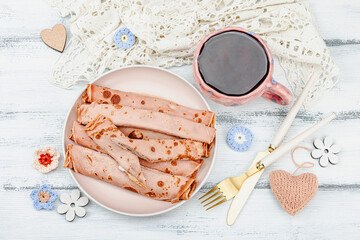 A cup of fragrant hibiscus tea and thin pancakes with cream. Good mood concept, cozy home comfort