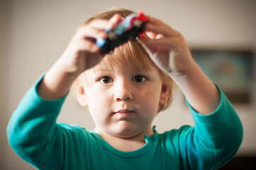A young child focuses intently while holding a toy car, engaging in imaginative play at home. The cozy indoor setting enhances the warmth of the moment, showcasing joy and curiosity