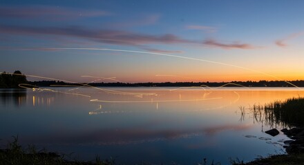 Serene sunset over a tranquil lake with light trails from passing boats