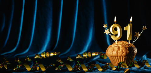 Number 91 gold celebration candle and small stars in sweet cupcake on bright blue velvet background. Concept of celebrating birthday, anniversary. Banner.