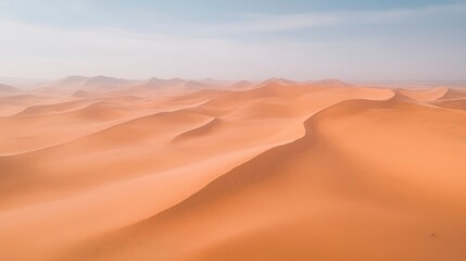 Fototapeta na wymiar Aerial view of vast, orange sand dunes under a hazy sky.