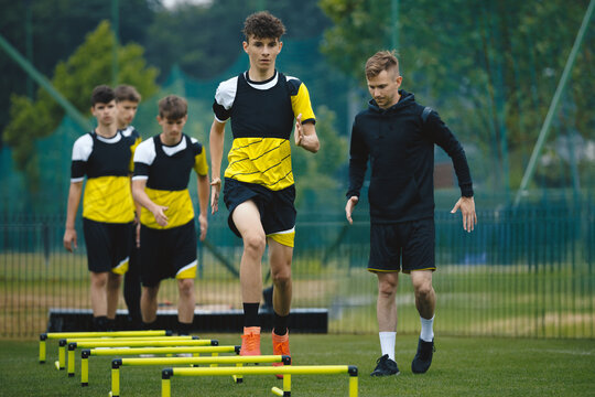 Teenagers on soccer training camp. Boys practice football with young coaches. Junior-level athletes improving soccer skills on outdoor training. The player runs over ladder-skipping and hurdles