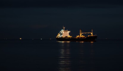 Fototapeta premium Cargo ship illuminated at night on ocean. Marine transportation, trade, logistics, and sustainability.