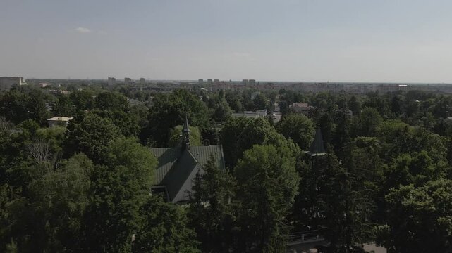 Aerial view of a suburban area with dense green trees, scattered houses, and church spires under a clear sky

