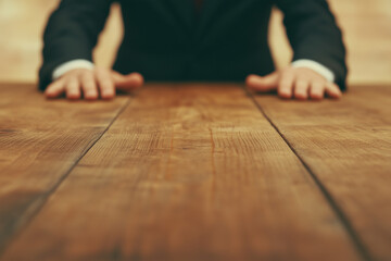 businessman sitting at wooden table with hands visible creating perspective view of rustic conference surface with focus on grain texture