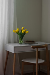 A cozy workplace - a bouquet of yellow tulips, a laptop, a notebook on a white table