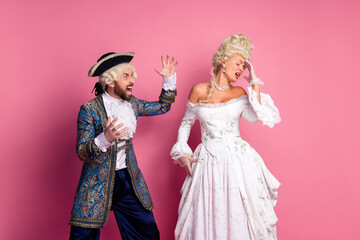 Elegant couple in vintage costumes posing dramatically on pink studio background