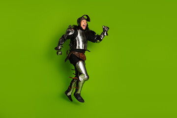 Young man dressed as a medieval knight jumping in armor on a green background